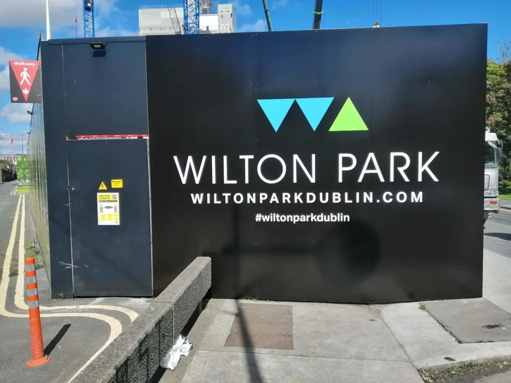 Wilton Park construction site hoarding in Dublin with logo and website address visible.