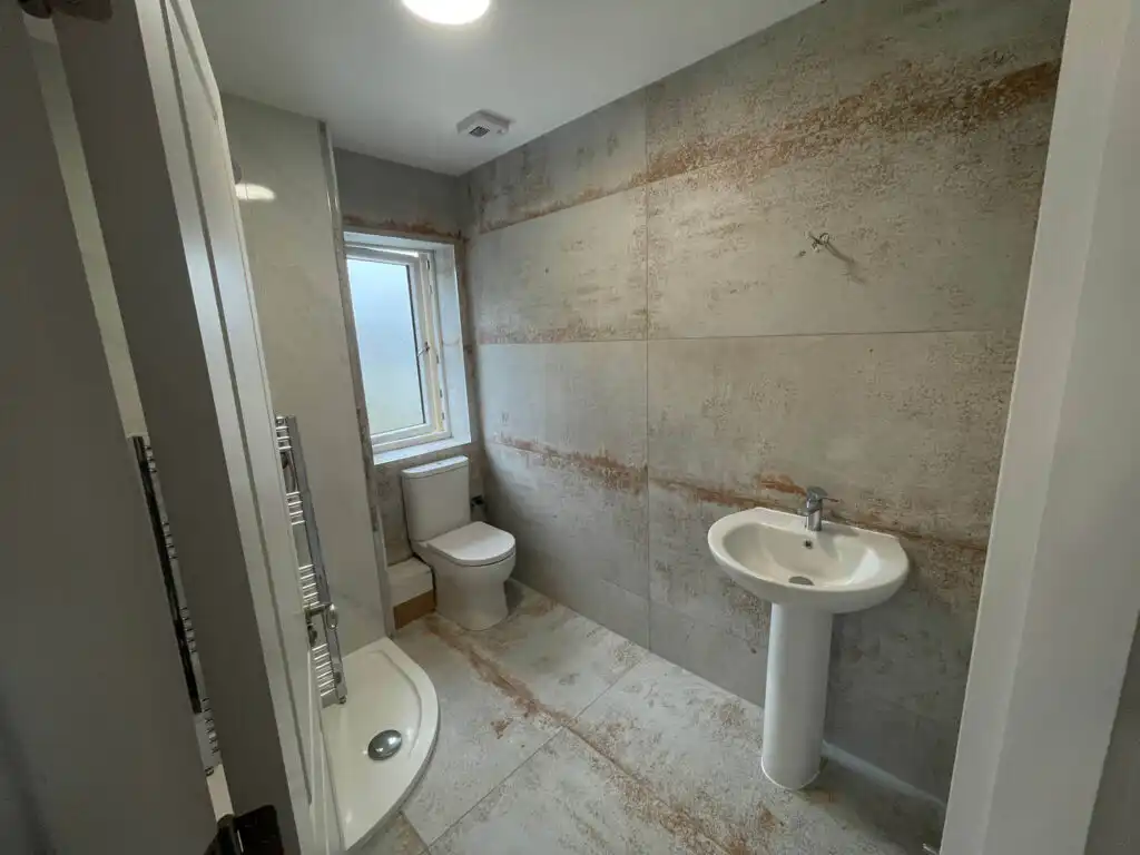Modern bathroom with shower, toilet, and sink, featuring textured tile walls.